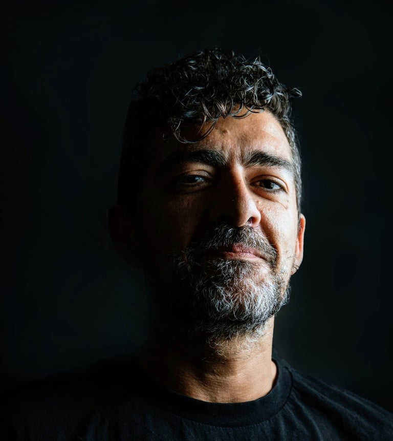 Portrait of a man with beard and curly dark hair against a dark background, wearing a black shirt