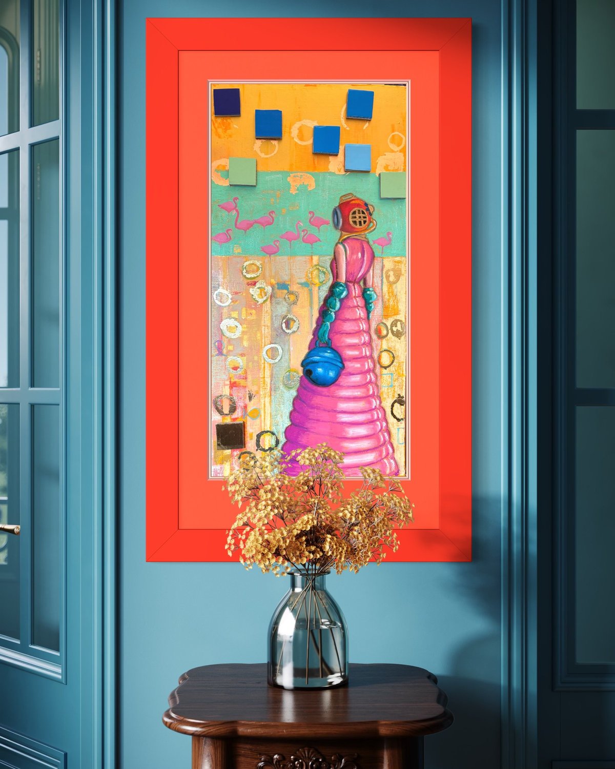 Colorful abstract mixed media artwork in red frame hanging above wooden table with glass vase of golden dried flowers